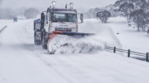 A powerful snow plow truck clearing a snow-covered road in a serene winter landscape.